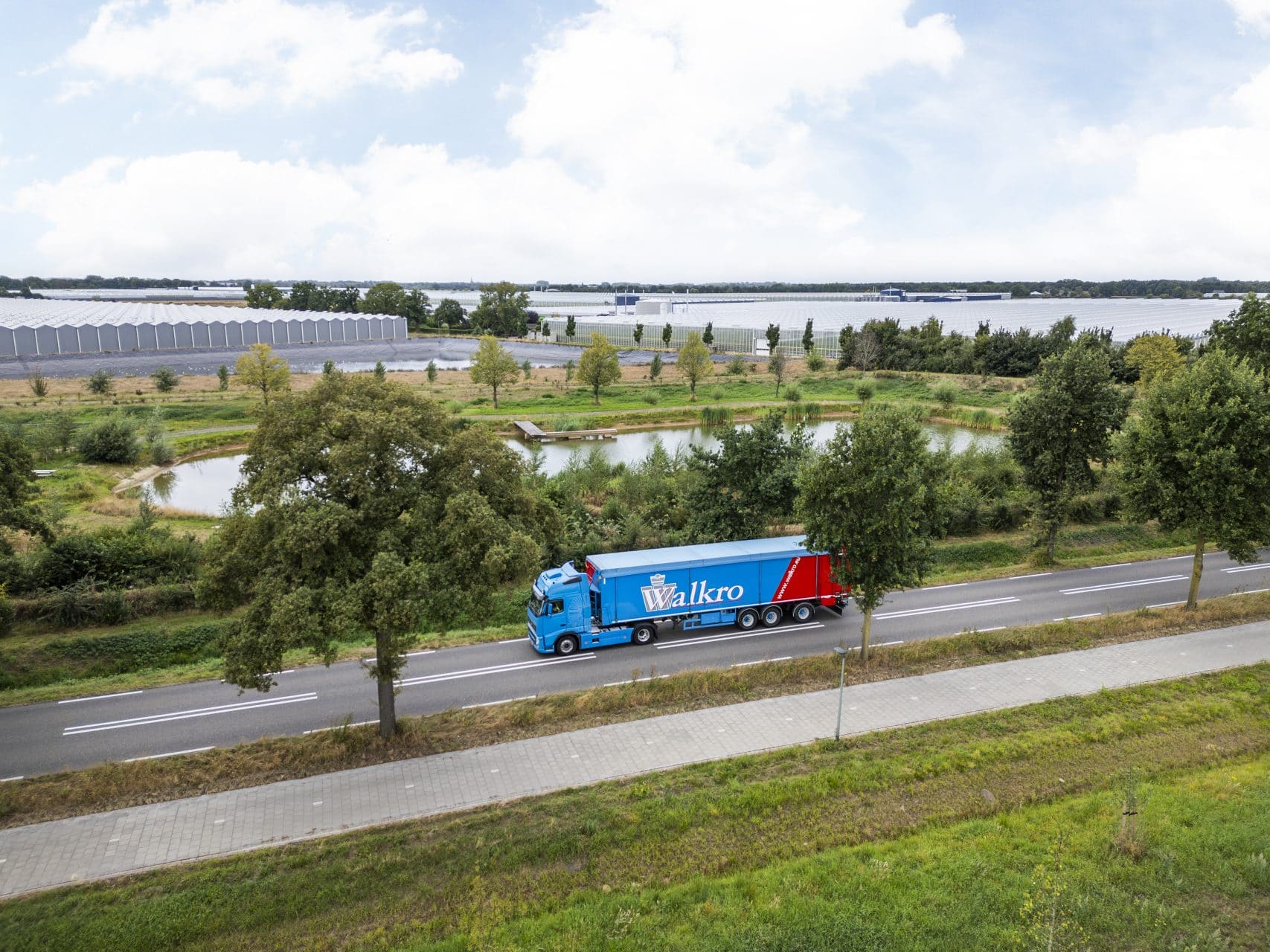 Walkro truck drives through green landscape with water and trees.