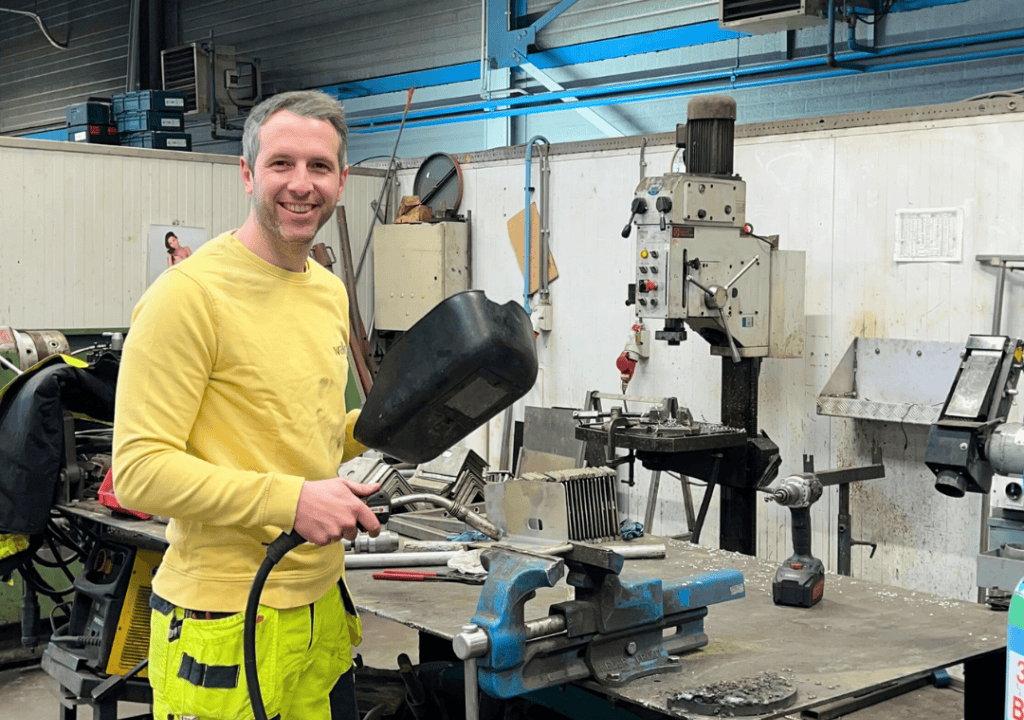 Onderhoudstechnieker met lashelm bij machine in werkplaats.