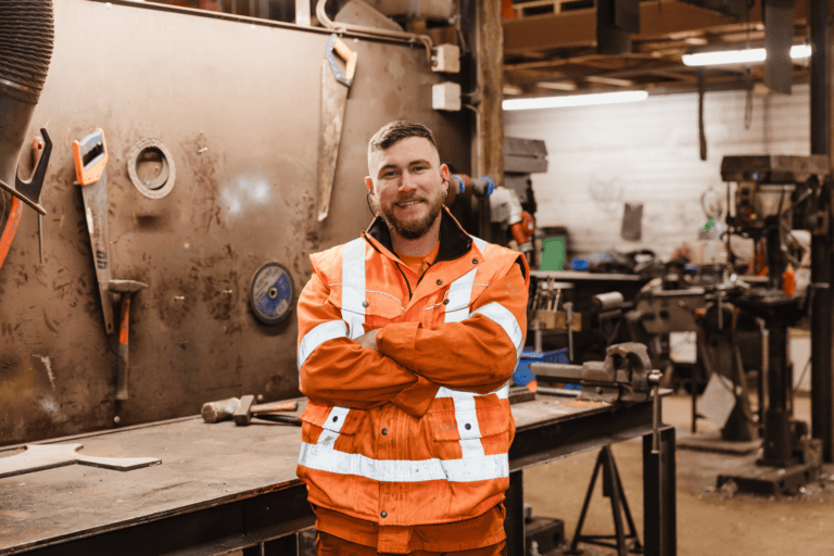 Werkplaats medewerker in veiligheidskleding in een werkplaats met gereedschap en machines.